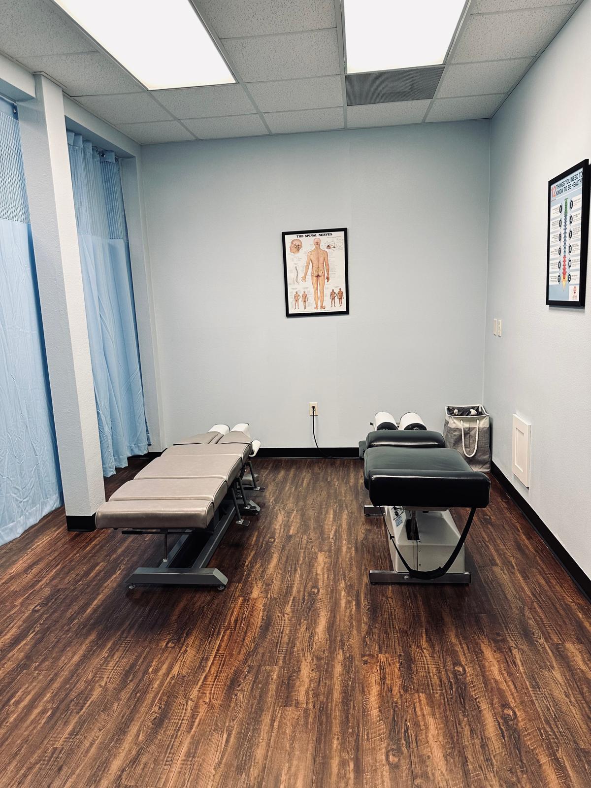 An upper cervical care treatment room at the Atlas Injury to Health center in Ocala, Florida, with two adjustable tables and spinal nerve charts