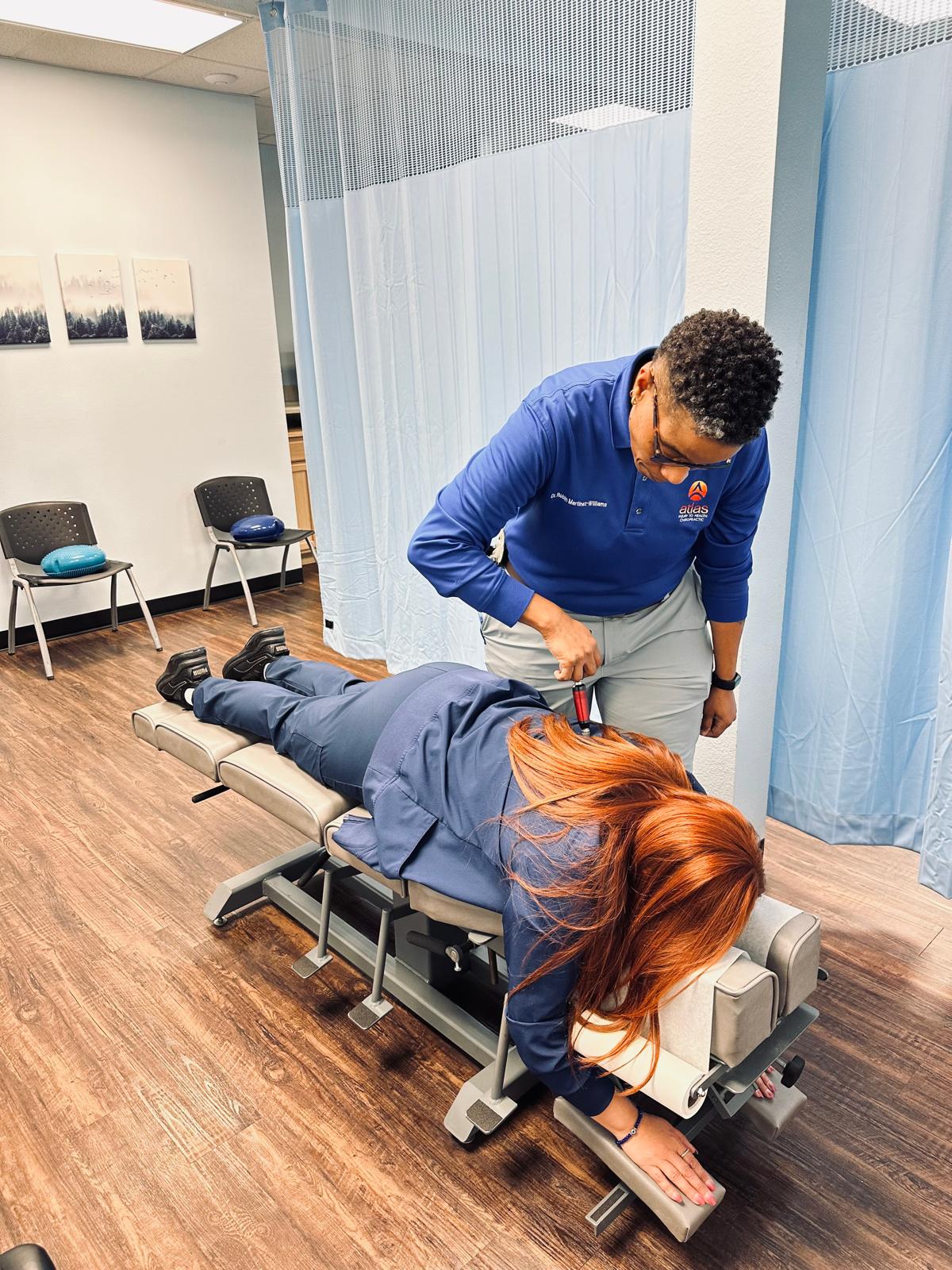 Atlas Injury to Health clinician uses a precision instrument for upper cervical care on a patient lying face-down on a treatment table