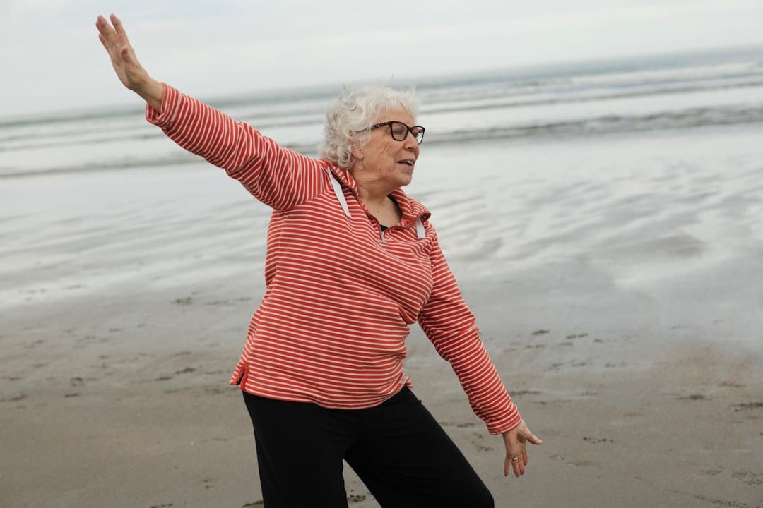An older woman with upright, open posture practicing tai chi on the beach — illustrating restored mobility and function through upper cervical care for kyphosis.