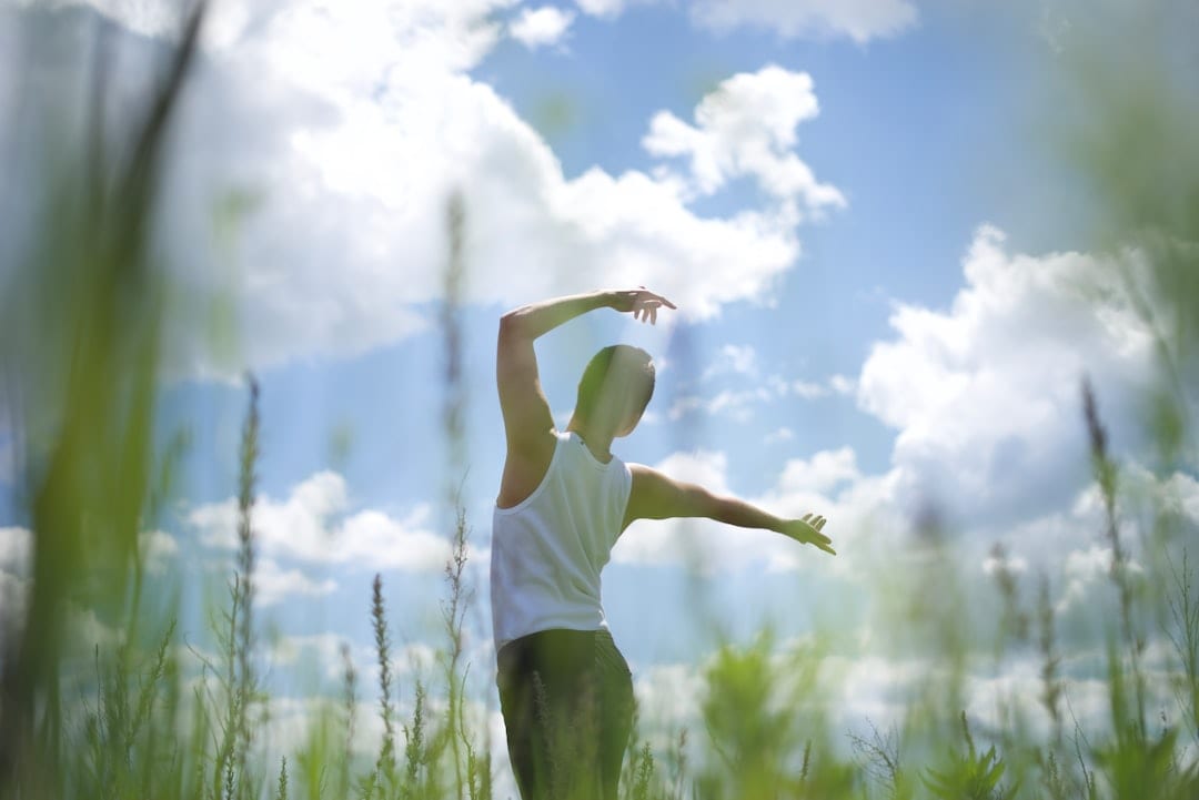 A person standing in an open field with arms raised toward a bright sky, reflecting the freedom and vitality that restored spinal alignment and metabolic wellness can bring.