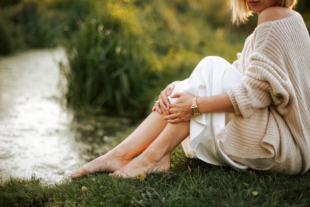 A woman sitting peacefully by a stream in a natural setting, reflecting the calm and restored sense of well-being that upper cervical care can bring to those managing neuropathy symptoms.