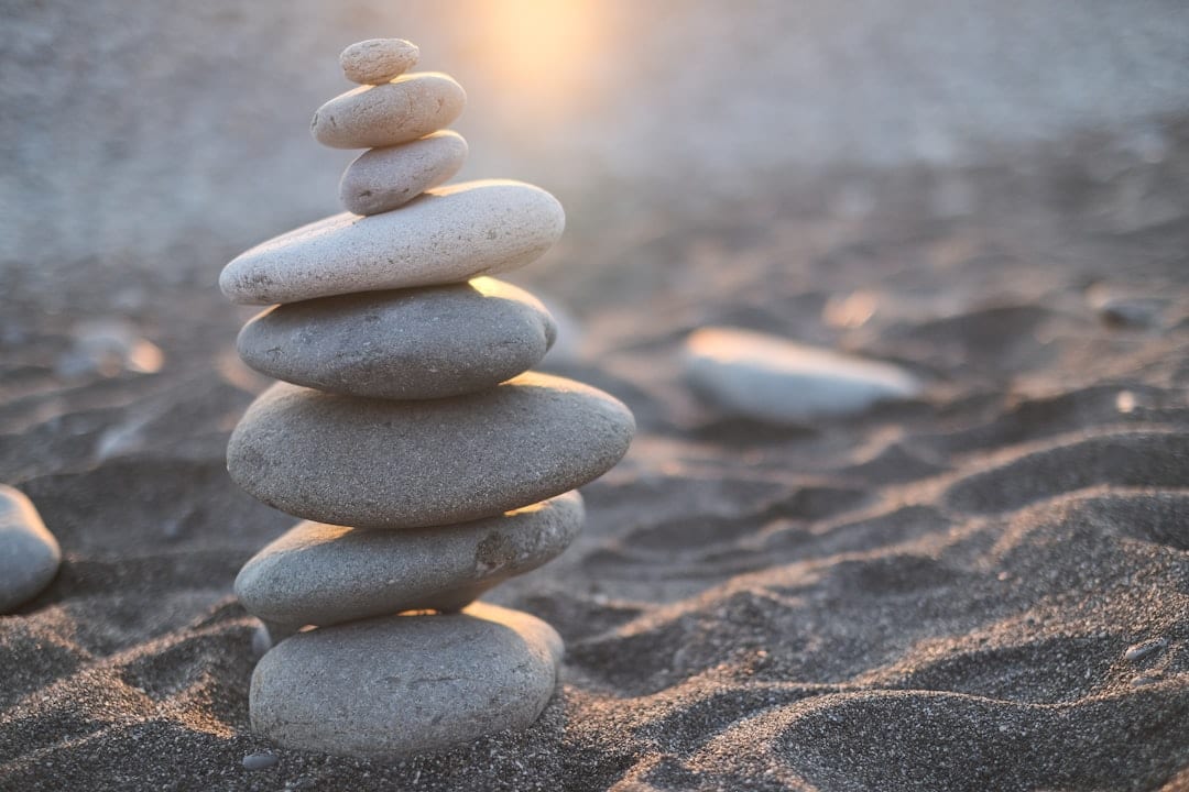 A serene stack of smooth white stones balanced on sandy ground, evoking the precision and restored balance at the heart of upper cervical care.
